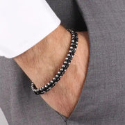 Bracciale in Acciaio rigido in corda nera intrecciata insieme a sferette in metallo lucido. Chiusura a scomparsa